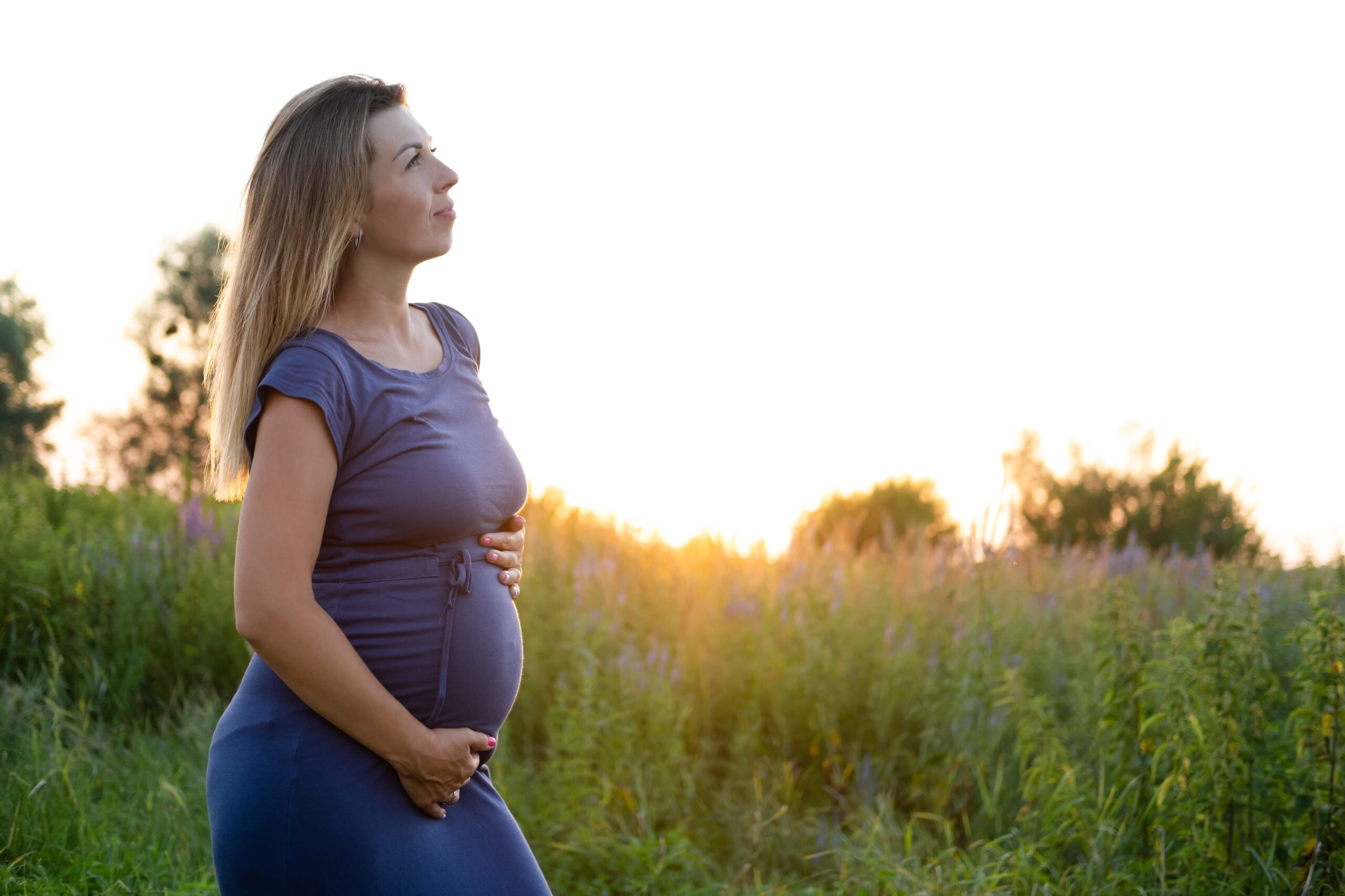 Happy healthy pregnancy and maternity. Portrait of pregnant young caucasian woman wearing long blue dress posing in park outside. Beautiful feminine expecting lady.